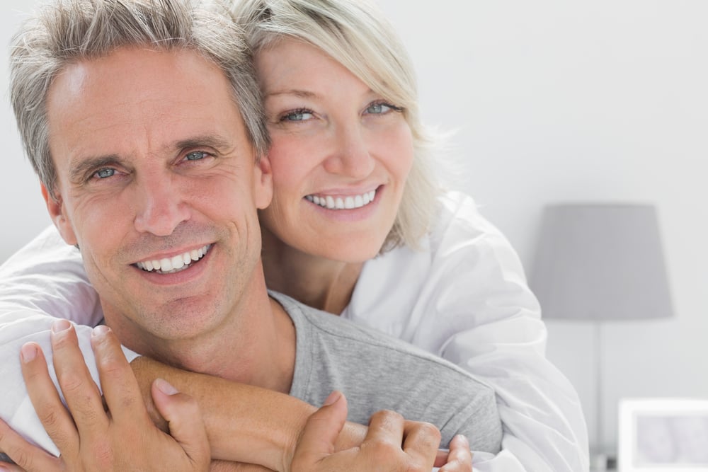 Affectionate couple smiling at camera at home in bedroom