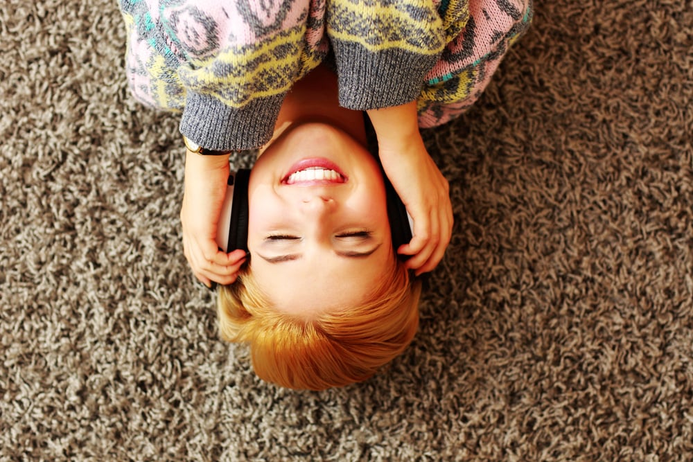 Cheerful young woman listening music in headphones at home