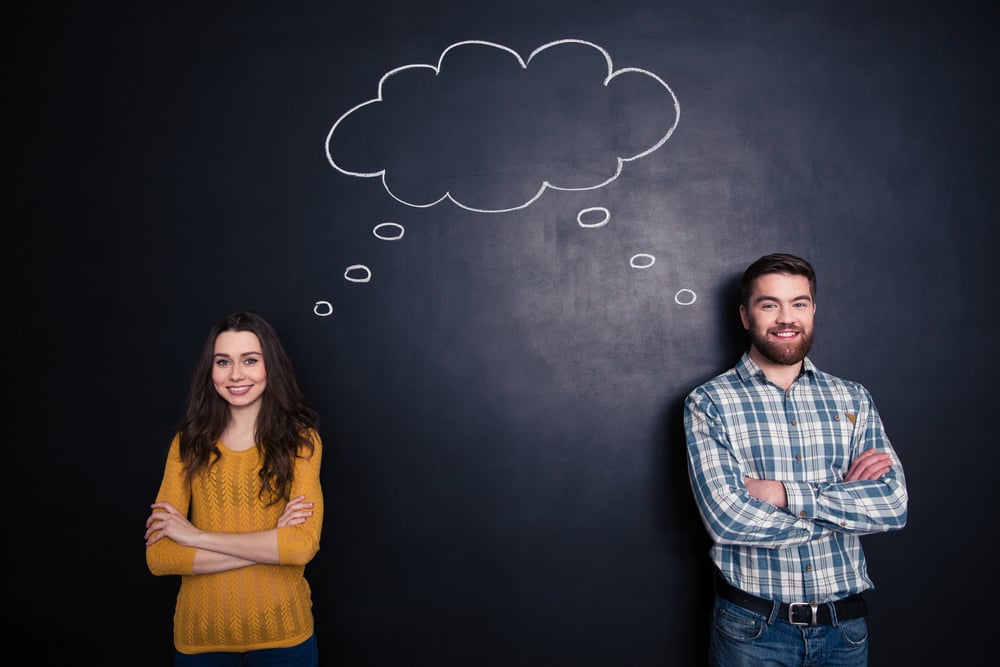 Happy couple standing with arms crossed and having the same thoughts over black board background