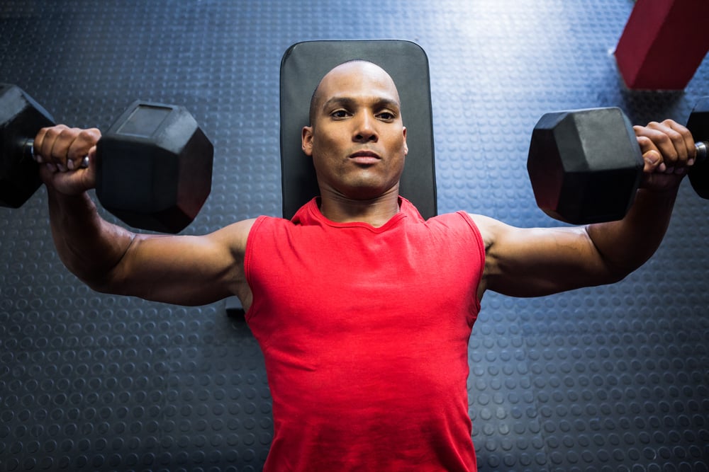 High angle view of male athlete exercising with dumbbells on weight bench