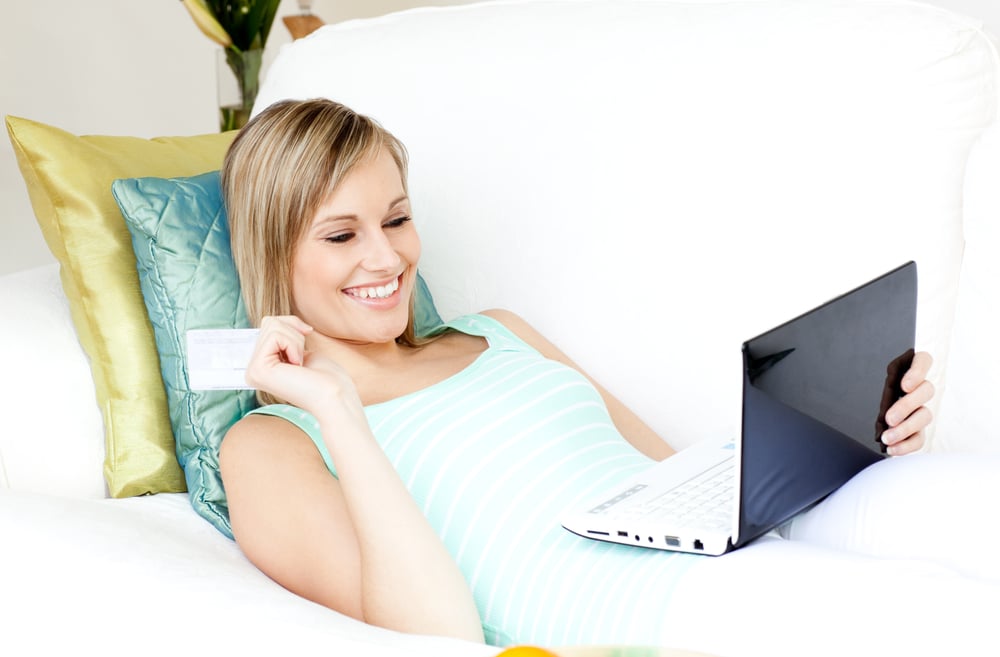 Jolly woman shopping on-line lying on a sofa at home