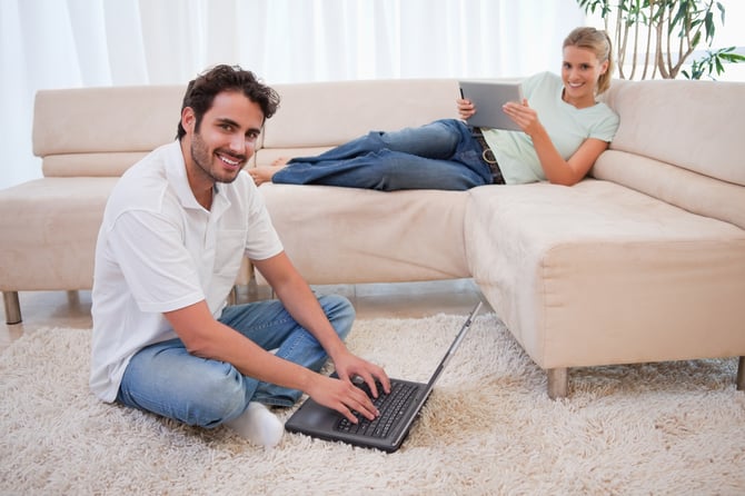 Woman using a tablet computer while her boyfriend is using a notebook in their living room